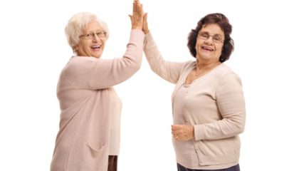 Two elderly women high-fiving each other and looking at the camera isolated on white background